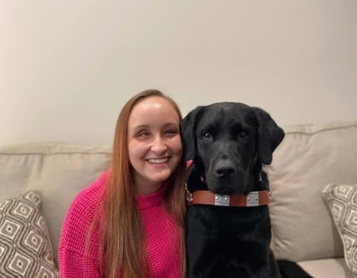 Founder, Zhenya Pankova, sits on a couch with Kingston, her black lab guide dog.