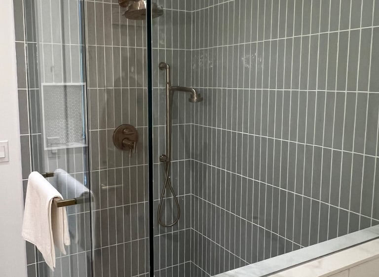 Modern walk-in shower featuring green vertical subway tiles and frameless glass door.