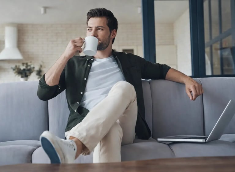 Professionnel détendu sur canapé avec café et ordinateur, ambiance hébergement professionnel