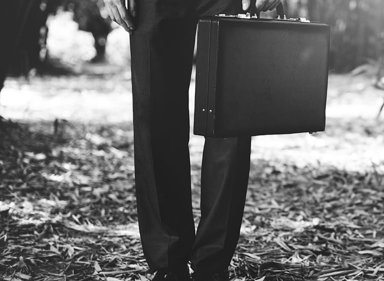 Foto a blanco y negro mostrando de la cintura para abajo un hombre con traje y maletín en mano.