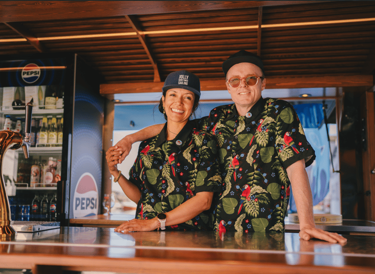 Maria og Ulrik i Maritime Munchies food truck, smiler bak disken med drikkevarer i bakgrunnen.