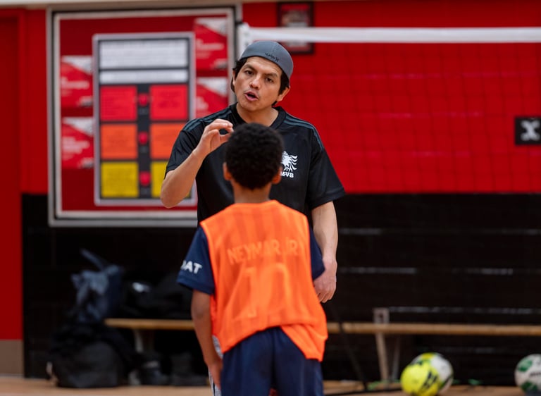 A MVB FC soccer coach instructs a young player indoor in Mississauga