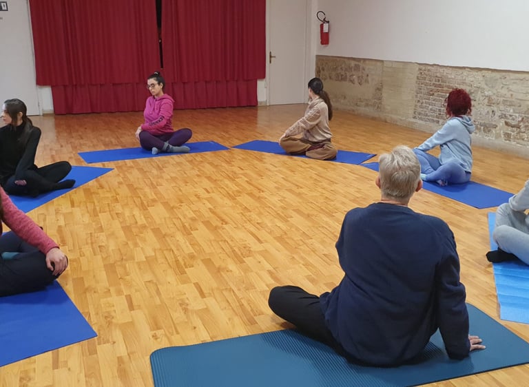 a group of people sitting on yoga mats in a circle, classe di esercizi di bioenergetica