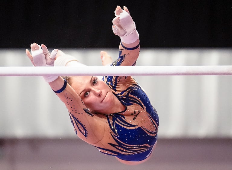 Gymnast performing a high-flying release move on the uneven bars at a gymnastics competition.