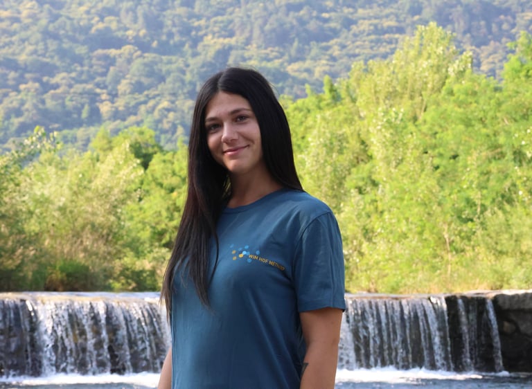 astrid mauri istruttrice certificata del metodo wim hof, davanti a una cascata con maglietta e logo 