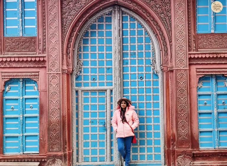 Person strolling past historic havelis in Bikaner with intricately carved doors and windows.