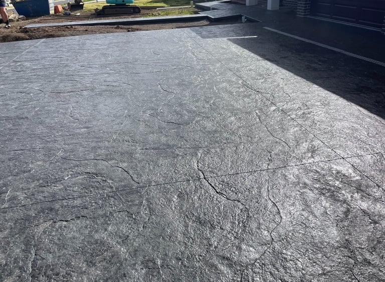 Dark gray stamped concrete driveway with a textured slate finish for a modern home exterior.