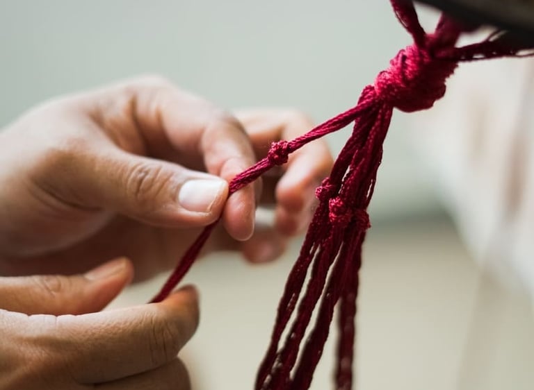 Manos elaborando un colgante de macramé con hilo de algodón rojo.