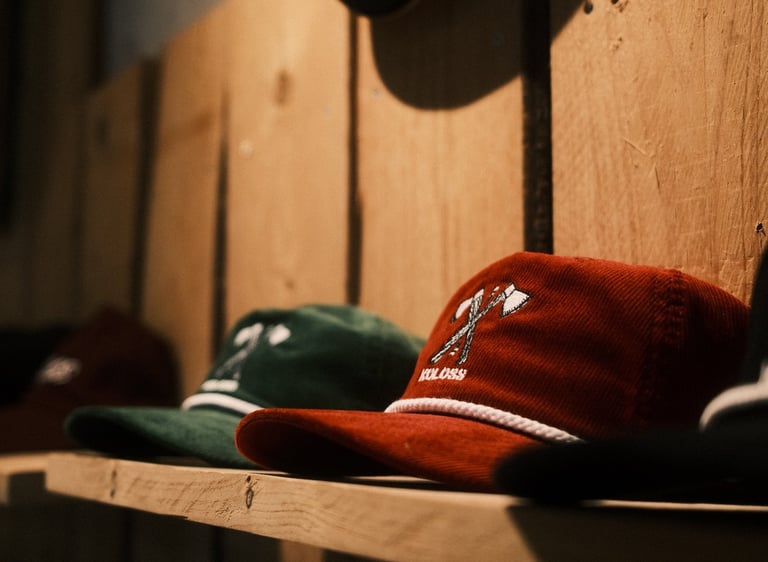 Produktfotografie Rheine: Rote und grüne Koloss Cord-Caps auf rustikalem Holzregal.