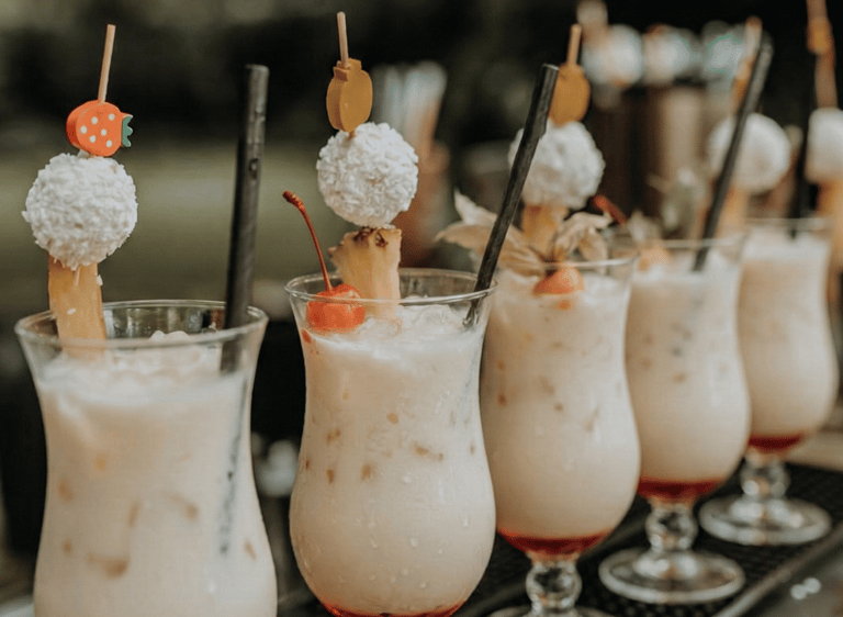 Tropical Pina Colada cocktails garnished with coconut balls and fruit skewers on a bar mat.