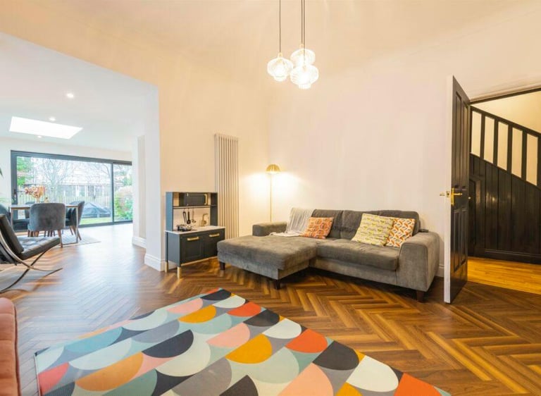 Modern living room with herringbone wood flooring, a grey corner sofa, and a colorful geometric rug.