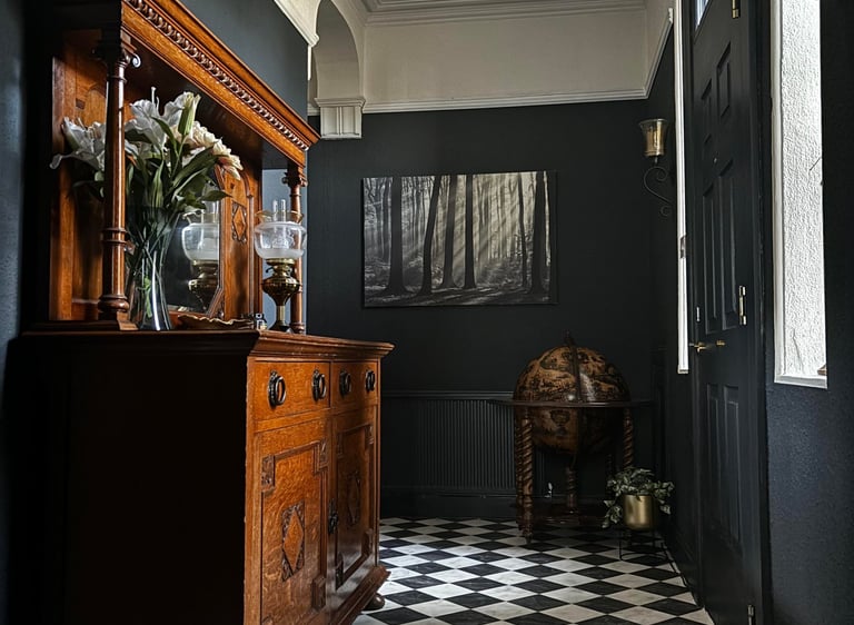 Elegant dark hallway with checkered floor, antique wooden sideboard, and crystal chandelier.