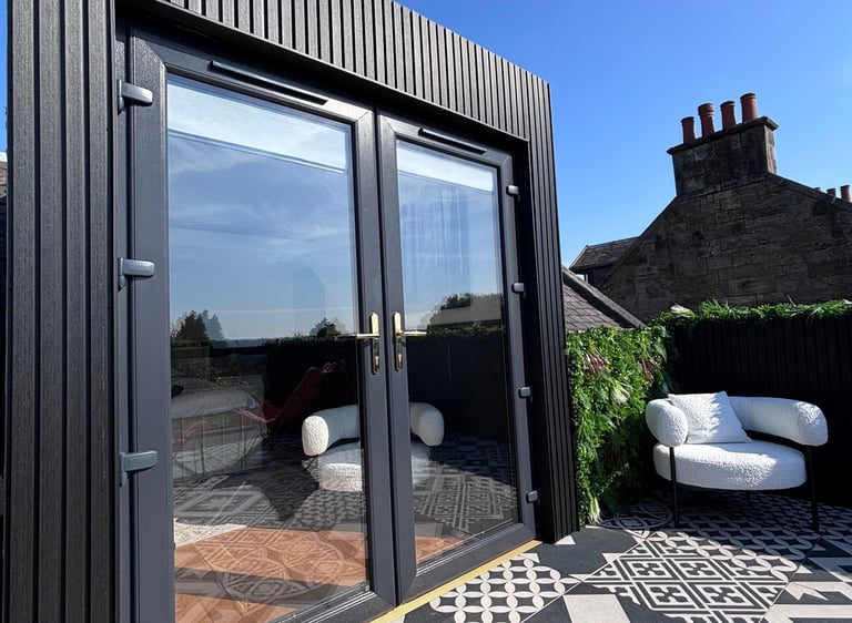 Modern rooftop balcony with black slat cladding and glass french doors on a patterned tile patio.