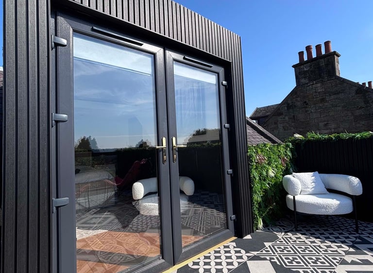 Modern rooftop terrace with black wood cladding, glass french doors, and patterned floor tiles.