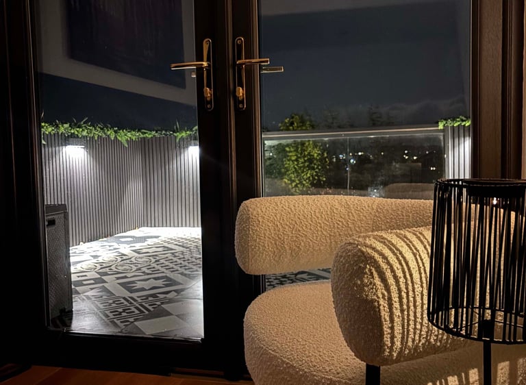 Modern white boucle armchair by glass balcony doors overlooking a lit outdoor patio at night.