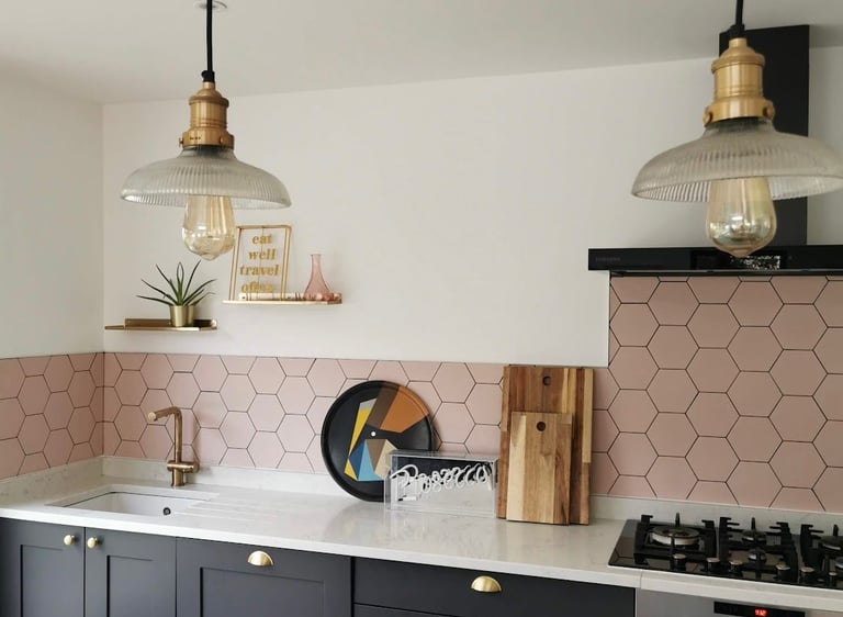 Modern kitchen featuring black cabinets, pink hexagon tile backsplash, and industrial glass pendant lights.