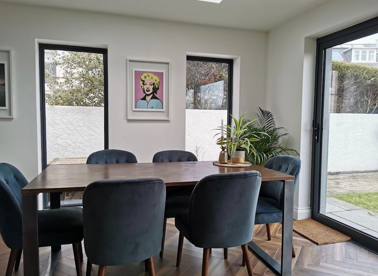 Modern dining room with a wooden table, blue velvet chairs, and pop art on a white wall.