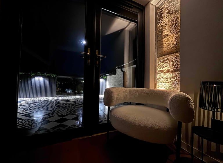 Modern white boucle armchair next to a black glass door overlooking a moonlit patio with geometric tiles.