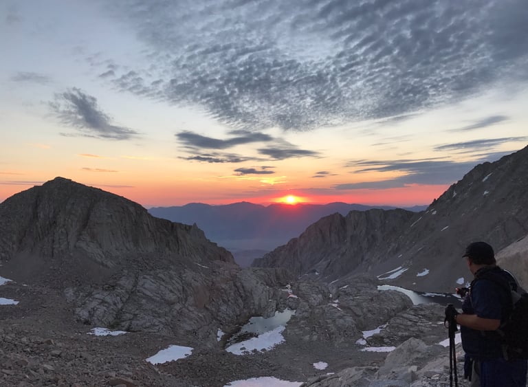 Sunrise from viewpoint on Mt Whitney with a hiker in foreground