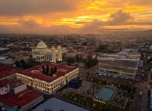 Aerial view of San Salvador city center at sunset featuring the National Palace and Metropolitan Cathedral.