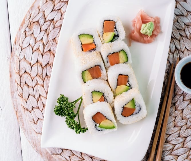 a plate of sushi rolls with chopsticks and sauce