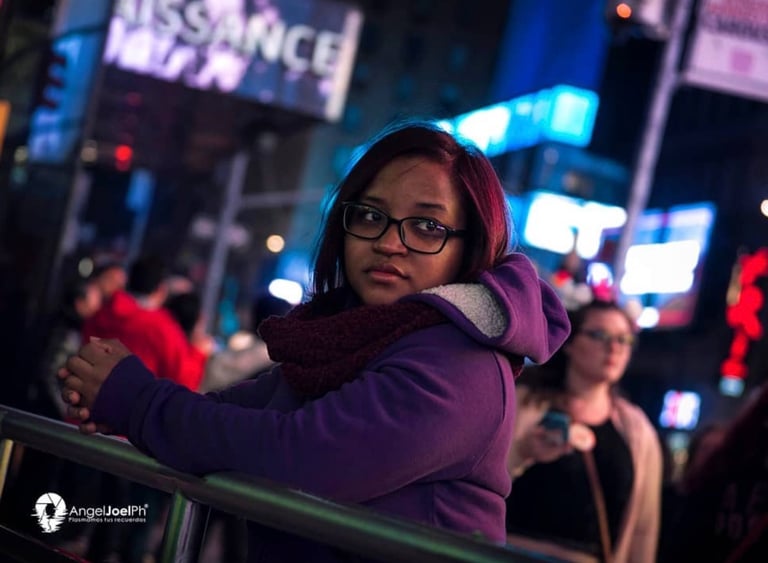 Retrato nocturno de una joven con abrigo morado y bufanda, en Times Square, Nueva York, rodeada de l
