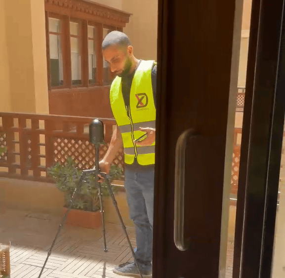 A surveyor in a yellow safety vest uses a 3D laser scanner on a tripod for a building site survey.