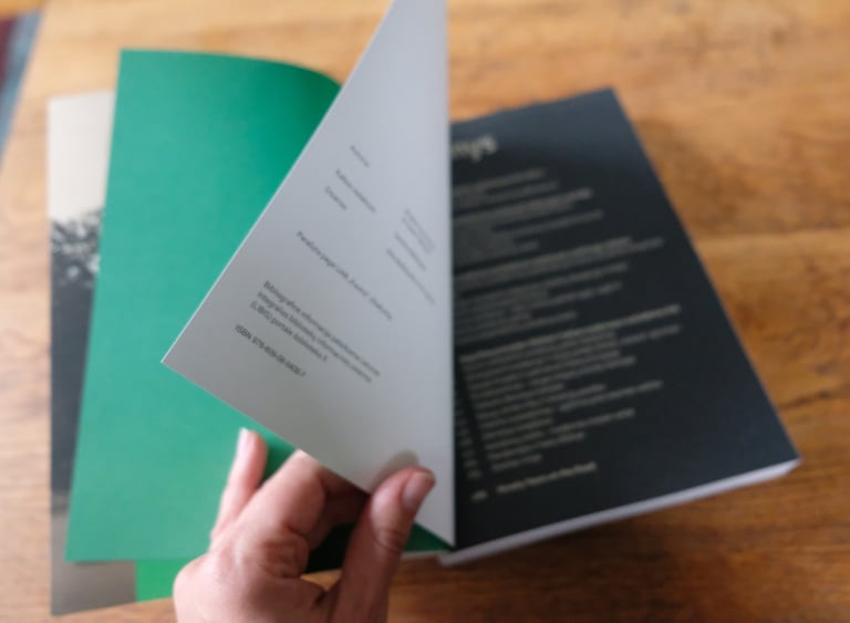 The photo shows the pages of a book being turned. The three main colours used in the book are asphalt grey, creamy white and 