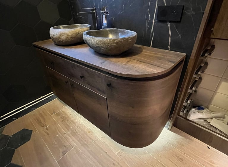 Modern bathroom vanity with double stone vessel sinks, wood cabinet, and black marble wall.