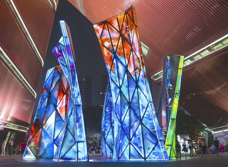 Blooming Sculpture lit up at night with its multi-colored glass panels and people walking around it