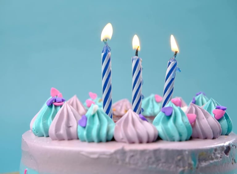 Torta de cumpleaños en tonos morado y azul, con velas encendidas y decoración de frosting en remolin