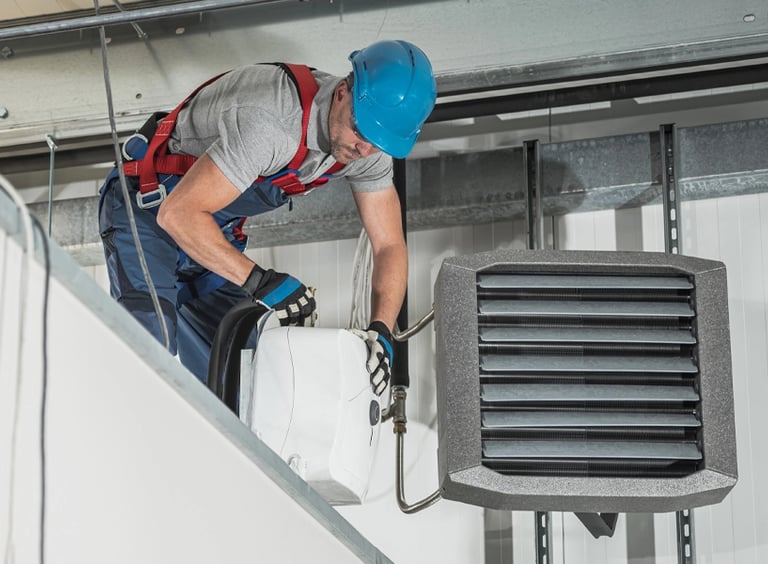 A HVAC technician in safety gear installs a commercial ceiling mounted air heater.