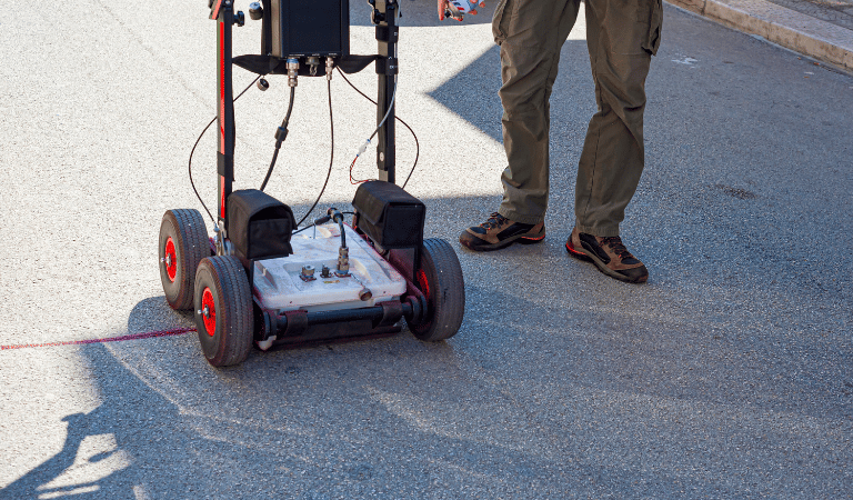Technician using a ground penetrating radar system for utility mapping on an asphalt road.
