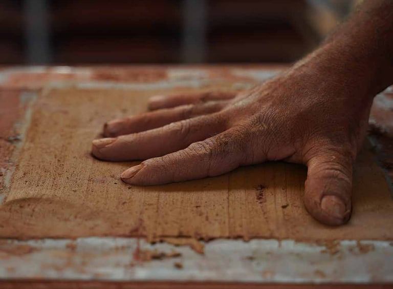 A potter's hand pressing and shaping a slab of raw terracotta clay in a ceramics studio.