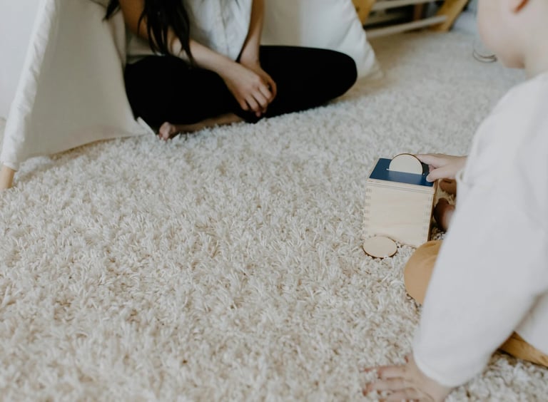A toddler plays with a wooden Montessori coin box toy on a plush rug near a play tent.