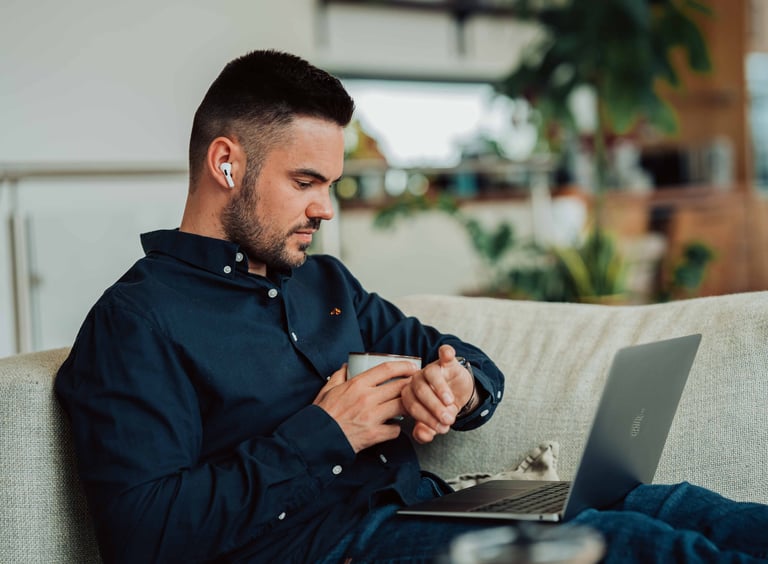 a man sitting on a couch with a laptop and a cell phone