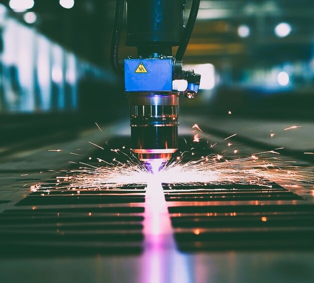 Industrial CNC laser cutting machine processing sheet metal with sparks in a factory.