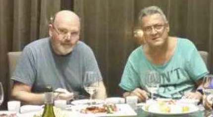 Two men enjoy a casual dinner with wine and shared appetizers at a restaurant table.