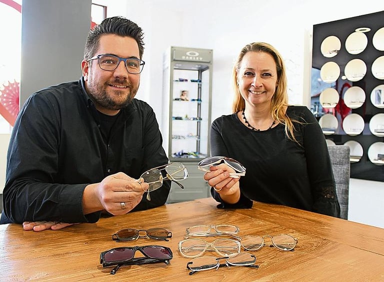 Gabi und Optiker halten jeweils eine Brille in der Hand.