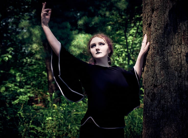 a woman in a black dress standing next to a tree dancing in the sunlight