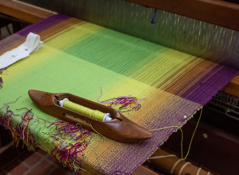 Weaving shuttle resting on an in-progess pieces warped on a loom.