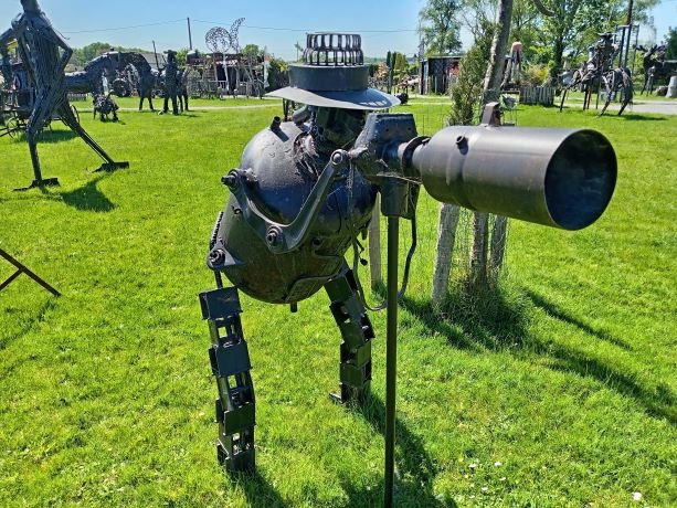 Metal scrap sculpture of a robot photographer with a camera in an outdoor art garden.
