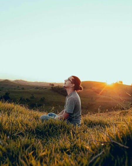 Person sitting in a field at sunset with head lifted in prayer.