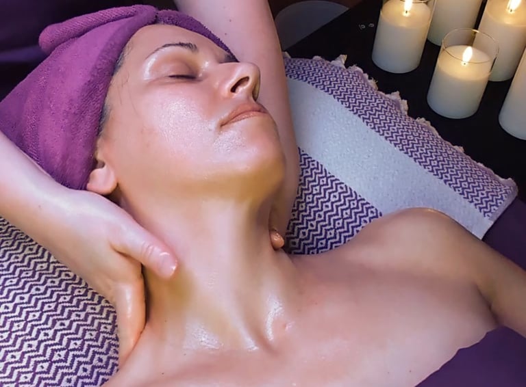 A woman receives a relaxing facial massage at a spa with lit candles in the background.