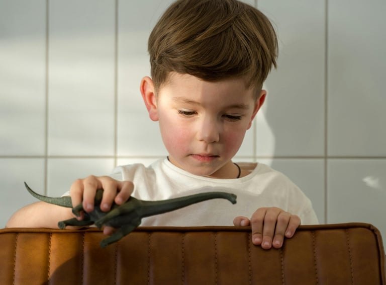 a young boy sitting in a suitcase with a dinosaur toy