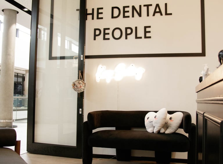 The Dental People office waiting area with tooth-shaped pillows on a black couch and neon sign.