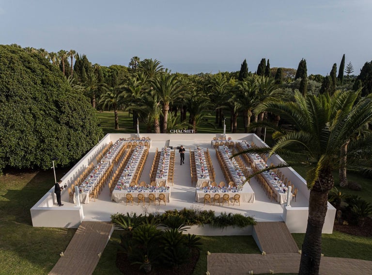 Luxury outdoor gala dinner setup for Chaumet with long formal tables and gold chairs in a Marbella.