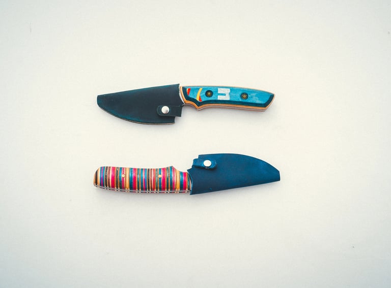 Two handmade fixed blade knives with colorful striped recycled skateboard wood handles and leather sheaths.