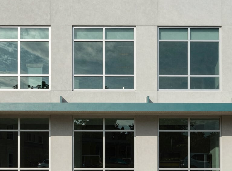 An architectural photography shot of a modern, accessible community building in North America. The facade features large windows and a clean light grey and teal color palette.