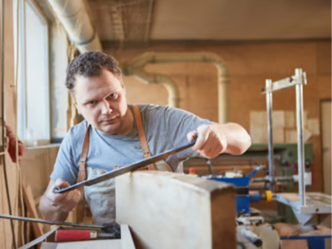 man with apron on using a drawknife on a piece of timber